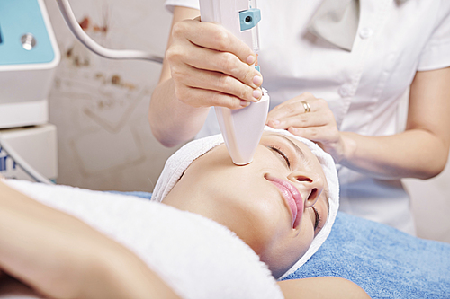 Smiling Caucasian young woman enjoying anti-aging procedure in beauty salon