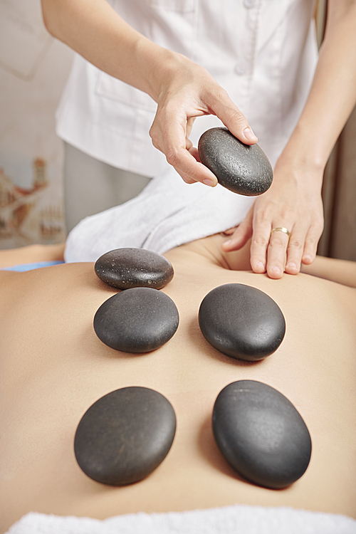 Close-up image of young woman receving relaxing hot stone massage in spa salon