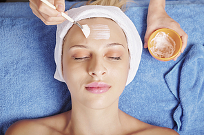 Close-up image of beautician using brush when applying natural mask on face of pretty female client