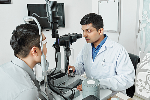 Indian ophthalmologist in white coat concentrating on his work he examining the eyesight of his patient during visit at hospital