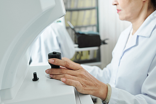 Close-up of female doctor holding the lever and using medical equipment while sitting and working at her office