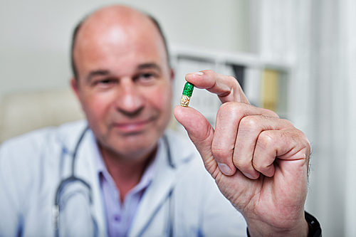 Green and yellow supplement pill in hand of general practitioner, selective focus