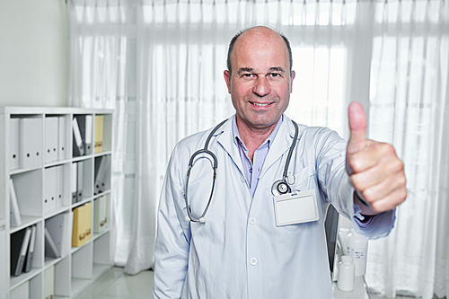 Portrait of happy mature doctor with badge on his labcoat showing thumbs-up