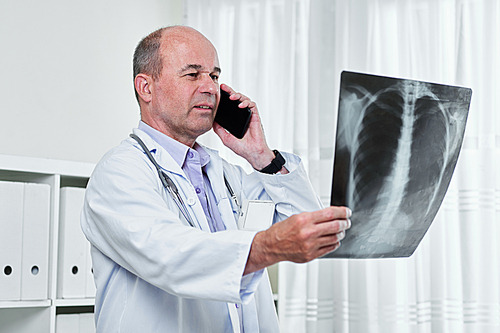 Serious general practitioner calling his patient when looking at chest x-ray
