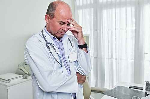 Stressed doctor standing in his office and thinking about difficult case he had at work