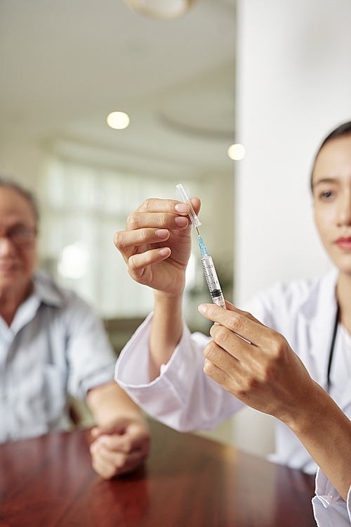 Close-up of female doctor holding syringe while making an injection to the patient at clinic