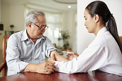 Asian female doctor in white coat making a vaccination from flu to the senior man while they sitting at the table