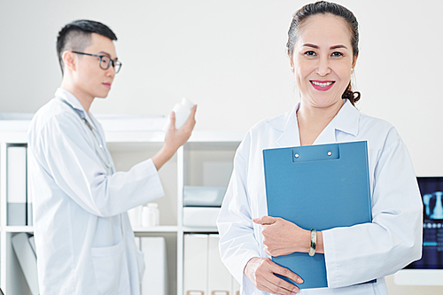 Cheerful mature Vietnamese doctor with clipboard smiling and 