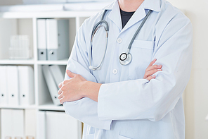 Cropped image of young doctor in white labcoat standing with his arms crossed in his office