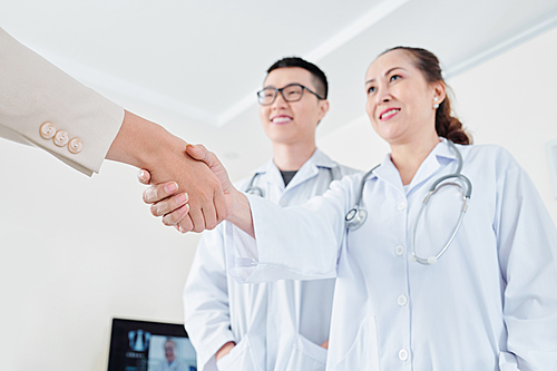 Female patient shaking hand of mature female doctor and his assistant, selective focus