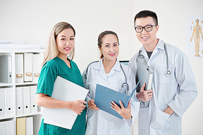 Team of Vietnamese medical workers in scrubs and labcoats posing with document folders