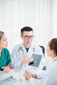 Smiling young Vietnamese neurologist showing tablet computer with brain x-ray and presenting new way of treatment to colleagues