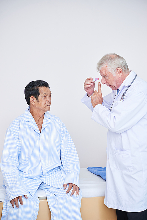 Experienced ophthalmologist talking to senior patient and explaining his how to uses eye drops