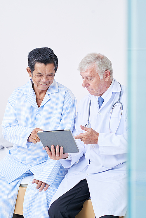 Physician showing tablet computer with prescription on screen to senior patient and explaining every point
