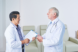 Senior multi-ethnic general practitioners in white lab coats talking in hall of medical clinic