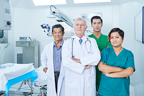 Team of confident multi-ethnic medical workers in uniform standing in operating room of clinic