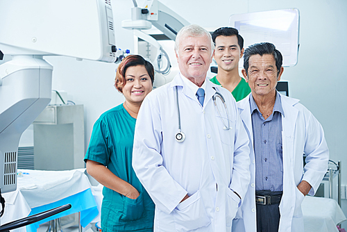 Smiling multi-ethnic group of doctors and surgeons standing in operating room of hospital