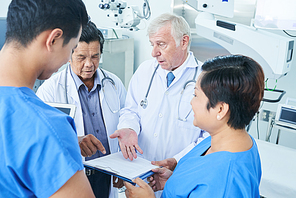 Group of doctors meeting in operating theater and discussing documents with medical tests of patient before surgery