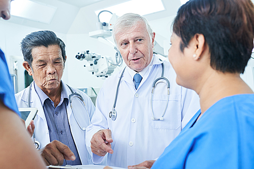 Group of doctors standing in operating room and discussing information in medical history of patient