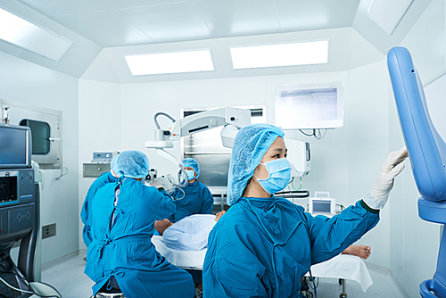 Asian nurse in scrubs setting program on computer for surgical equipment in operatin room