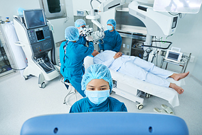 Vietnamese surgical assistant using computer to manipulate equipment above patient on bed and preparing for surgery