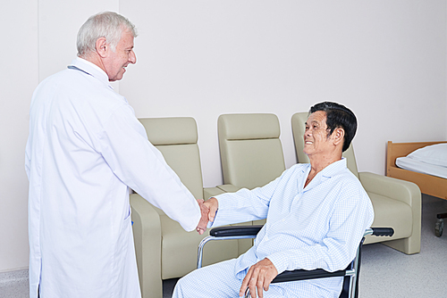 smiling doctor greeting senior vietnamese patient sitting on . and shaking his hand