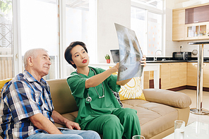 Young nurse showing chest x-ray of senior patient when visiting him at home