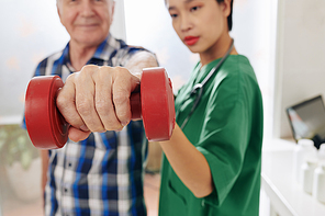 Smiling senior man doing exercises with dumbbells under control of medical nurse