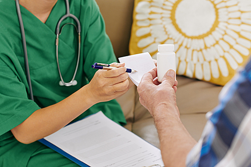 Close-up image of nurse giving bottle with medicine and prescription note to senior patient