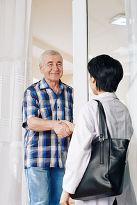 Smiling senior man shaking hand of doctor who is visiting him at home