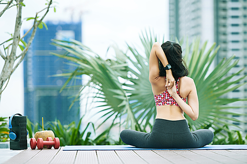 Rear view of young woman sitting on exercise mat and doing exercises outdoors
