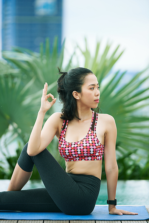 Young Asian woman in sports clothing sitting on exercise mat and relaxing on fresh air