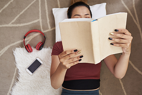 Young woman lying on the floor and reading students book, view from above