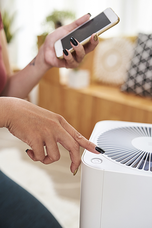 Hands of woman using mobile application to turn on fan in her room