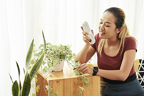 Young pretty Asian woman with speaker in her hands singing for house plants