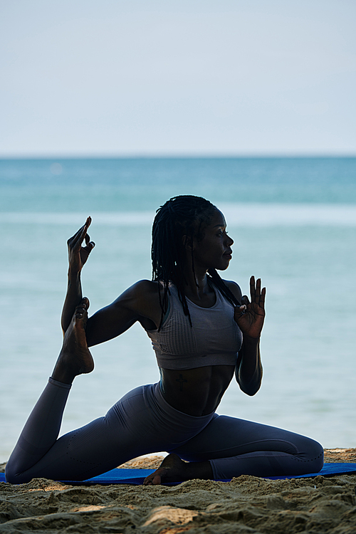 Young Black woman doing swan pose and making mudras when exercising on sandy beach