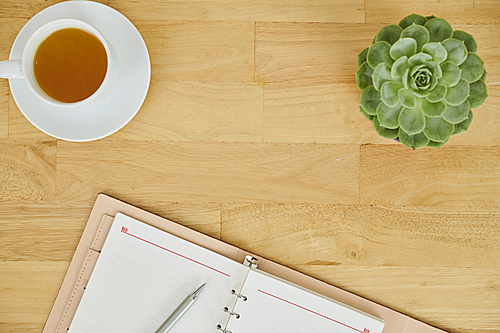 High angle view of wooden table with flower in pot cup of green tea and opened notepad for notes