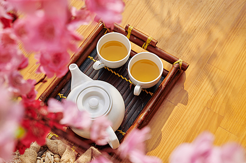 Two cups with herbal tea and pot on bamboo tray served for spring festival celebration