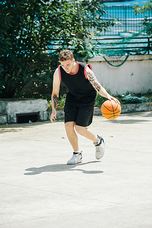 Young tall Caucasian man in black sports uniform playing backetball court outdoors