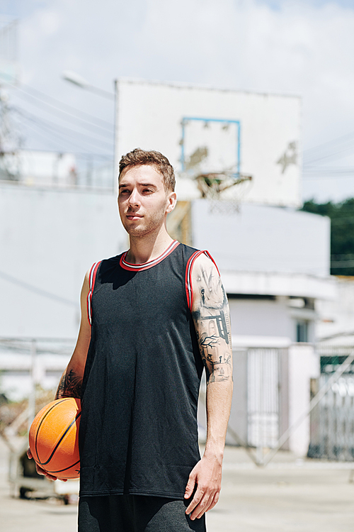 Portrait of handsome young basketball player standing on outdoor court with ball in hand