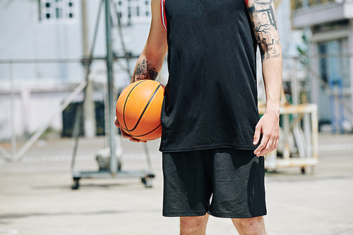 Cropped image of fit tall basketball player standing outdoors with ball on hot sunny summer day