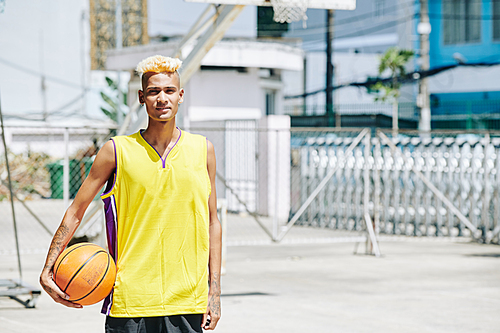 Portrait of Black handsome basketball player in bright yellow top posing on street basketball court