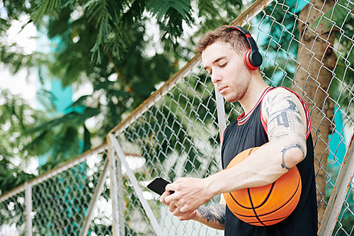 Serious young basketball player in headphones checking messages in his smartphone