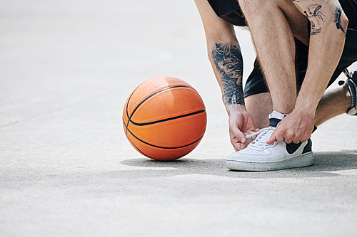 Close-up image of basketball player tying sports shoes on outdoor court