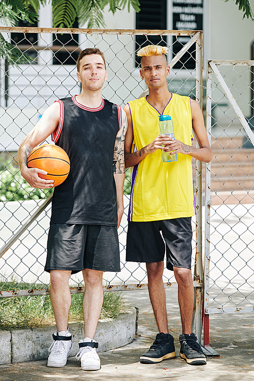 Full-length portrait of serious young handsome guys playing game of basketball on street court