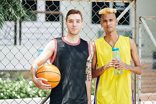 Portrait of happy young basketball players standing outdoors with bottle of fresh water and ball after game