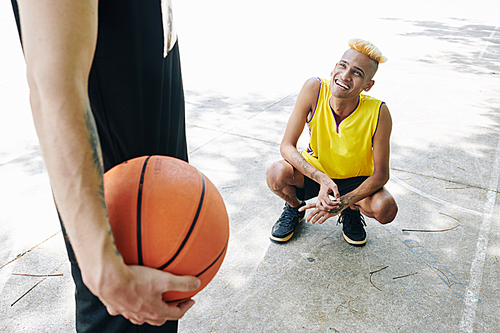 Smiling young man crounching down and looking up at his teammate with basketball ball in hand