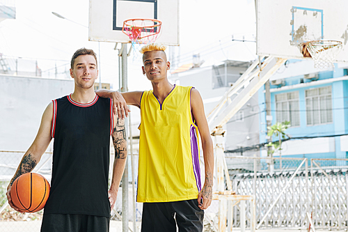 Smiling young multi-ethnic basketball players in uniform standing at street court and 