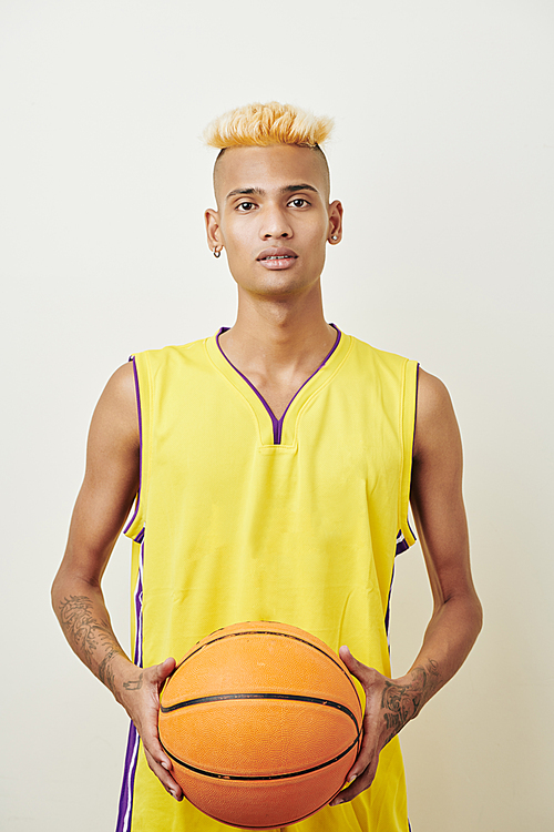 Portrait of handsome slim Black basketball player posing with ball against white background