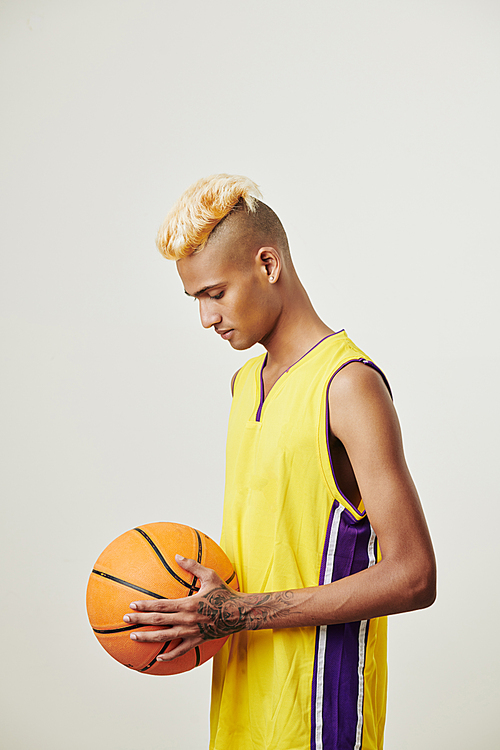 Pensive professional basketball player in bright yellow top looking at ball in his hands